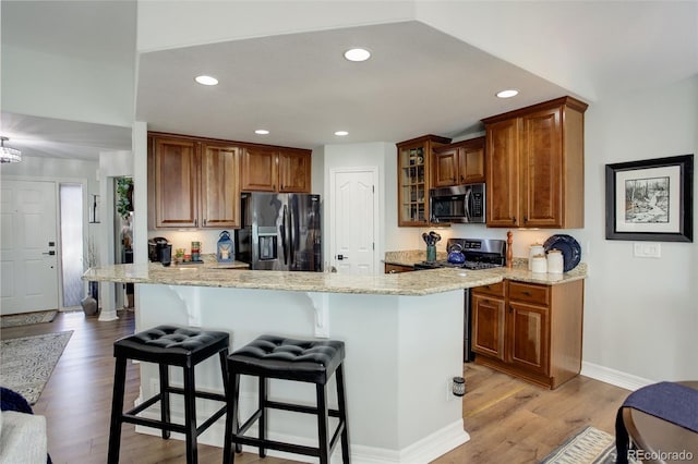 kitchen with glass insert cabinets, a breakfast bar, brown cabinets, stainless steel appliances, and light wood-type flooring