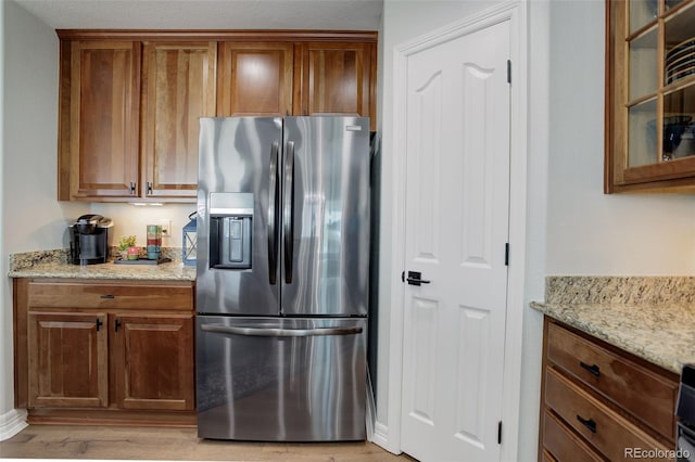 kitchen with light wood-type flooring, stainless steel refrigerator with ice dispenser, glass insert cabinets, and light stone countertops