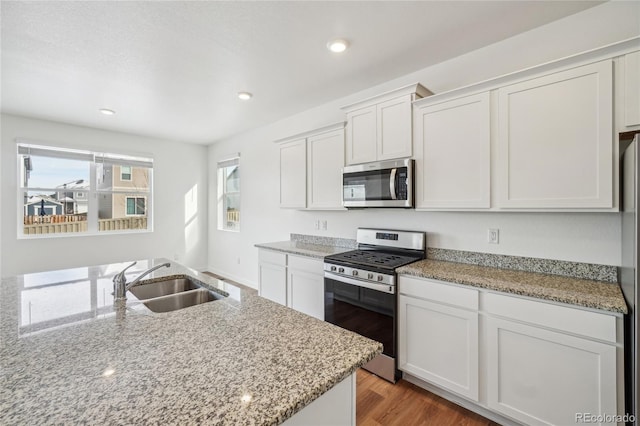 kitchen with sink, appliances with stainless steel finishes, light stone countertops, hardwood / wood-style floors, and white cabinets