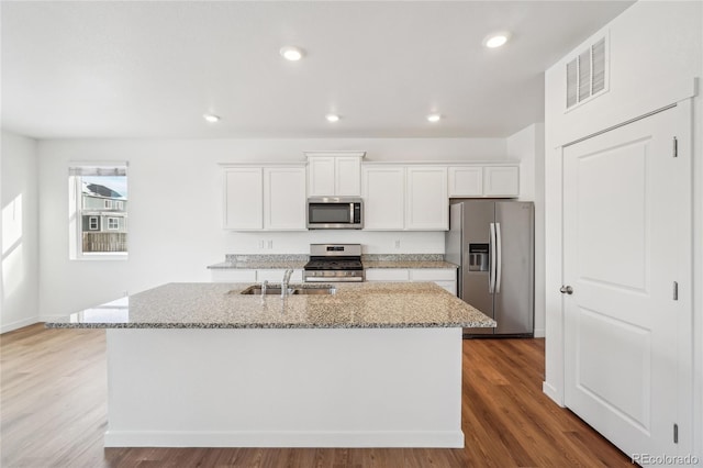 kitchen with white cabinetry, light stone counters, stainless steel appliances, and a center island with sink