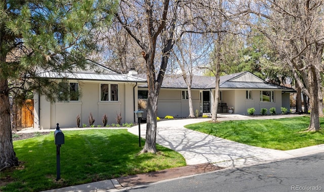 single story home featuring a front lawn, stucco siding, a chimney, and a standing seam roof