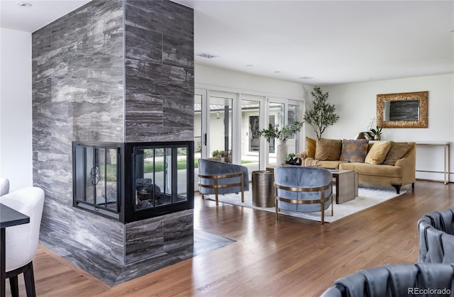 living room with wood finished floors, a baseboard heating unit, a wealth of natural light, and a fireplace