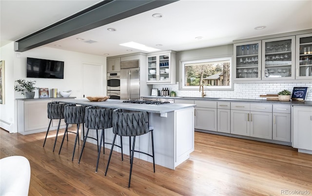 kitchen with backsplash, appliances with stainless steel finishes, a sink, light wood finished floors, and a breakfast bar