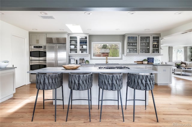 kitchen featuring appliances with stainless steel finishes, visible vents, a center island, decorative backsplash, and gray cabinetry