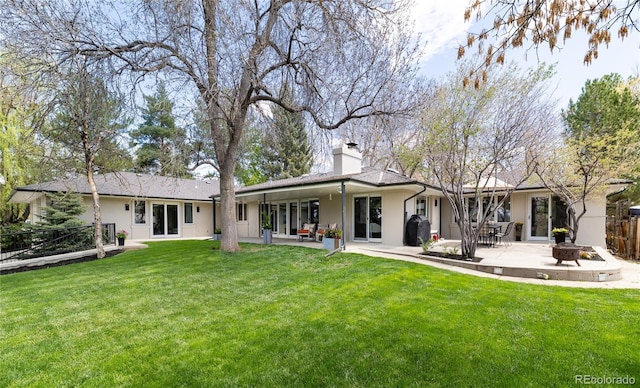 rear view of property featuring fence, a chimney, a yard, and an outdoor fire pit