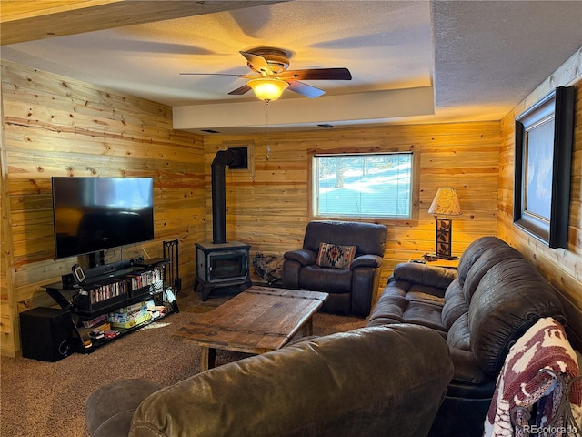 living room featuring a textured ceiling, carpet floors, ceiling fan, and a wood stove