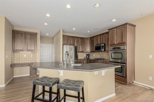 7852 Solstice Way, Castle Rock, CO 80108 - kitchen with stainless steel appliances, a breakfast bar area, light wood-type flooring, a sink, and tasteful backsplash