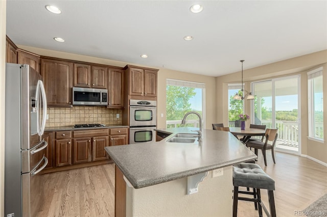 7852 Solstice Way, Castle Rock, CO 80108 - kitchen with appliances with stainless steel finishes, a sink, light wood-style flooring, a center island with sink, and recessed lighting