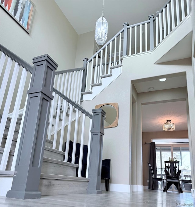 stairs with an inviting chandelier, a towering ceiling, and hardwood / wood-style flooring