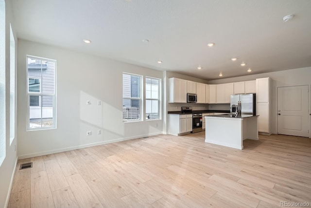 kitchen featuring white cabinets, stainless steel appliances, light hardwood / wood-style floors, and an island with sink