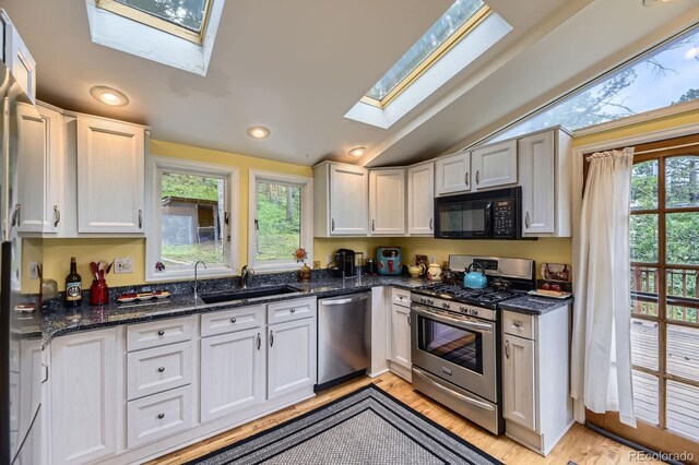 8758 S Murphy Gulch Rd, Littleton, CO 80127 - kitchen featuring appliances with stainless steel finishes, a skylight, lofted ceiling, light wood-type flooring, and white cabinetry