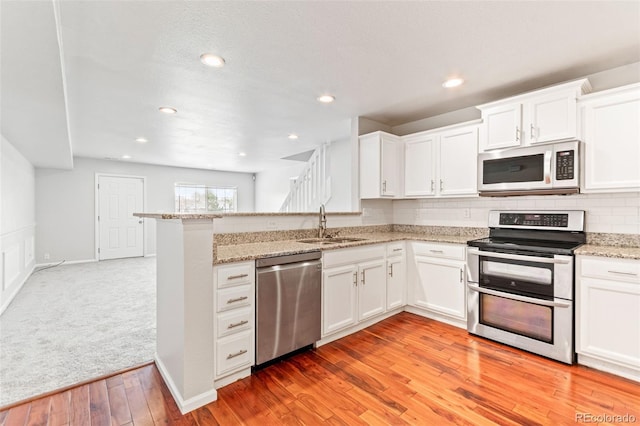 1461 S Danube Way Unit 104, Aurora, CO 80017 - kitchen with a sink, light wood-style floors, stainless steel appliances, white cabinetry, and a peninsula