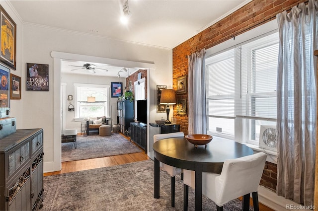 dining room with a healthy amount of sunlight, ceiling fan, brick wall, and hardwood / wood-style floors