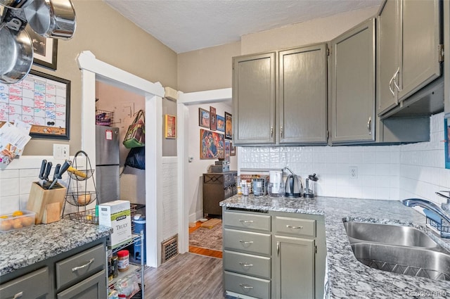 kitchen with light stone counters, a textured ceiling, sink, gray cabinetry, and hardwood / wood-style floors