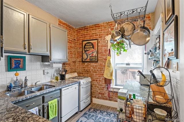 kitchen featuring sink, white appliances, brick wall, dark stone countertops, and light hardwood / wood-style floors