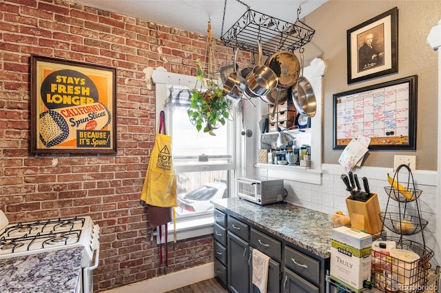 kitchen featuring a textured ceiling, dark wood-type flooring, white range with gas cooktop, brick wall, and stone countertops