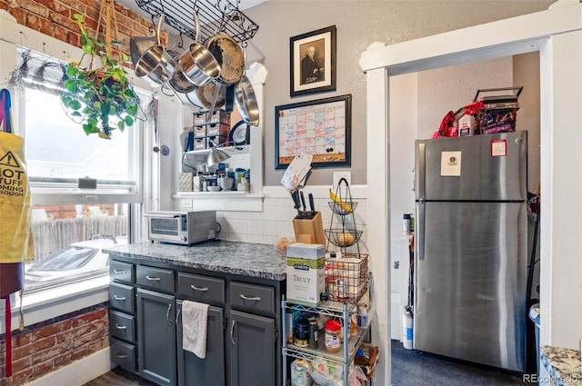 kitchen featuring brick wall, gray cabinets, dark stone counters, and stainless steel fridge