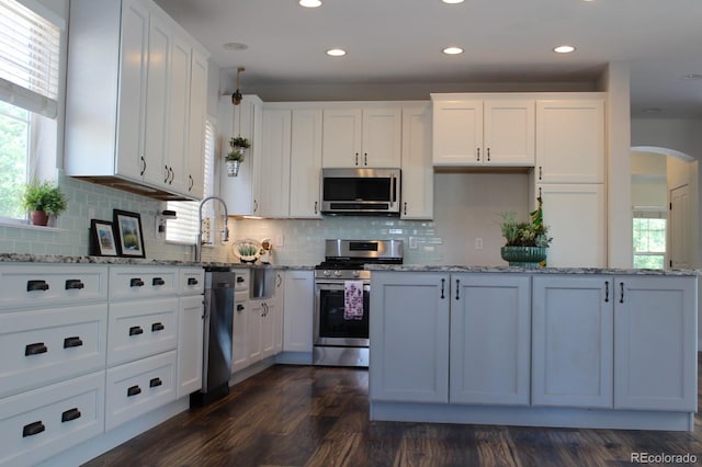 kitchen with tasteful backsplash, white cabinets, dark hardwood / wood-style floors, and appliances with stainless steel finishes