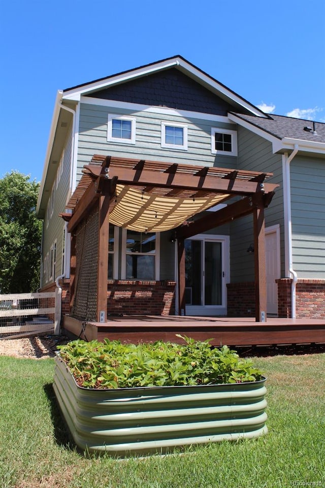 rear view of house featuring a pergola, a wooden deck, and a lawn