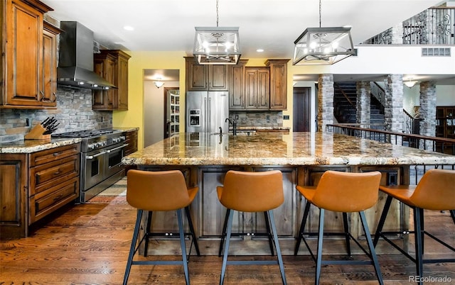 kitchen with a spacious island, wall chimney range hood, stainless steel appliances, and tasteful backsplash