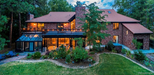 rear view of property featuring a patio area, a tiled roof, a chimney, and a yard