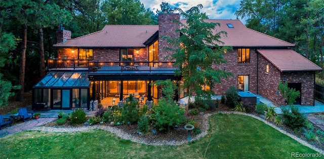 back of house with a chimney, a lawn, a tiled roof, a patio area, and a sunroom