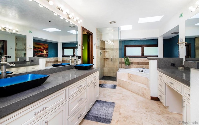 full bathroom featuring a sink, a skylight, a stall shower, double vanity, and a garden tub