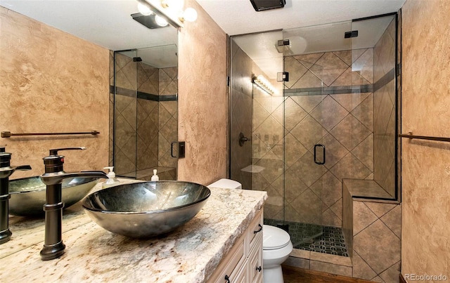 full bathroom featuring vanity, toilet, a textured wall, and a shower stall
