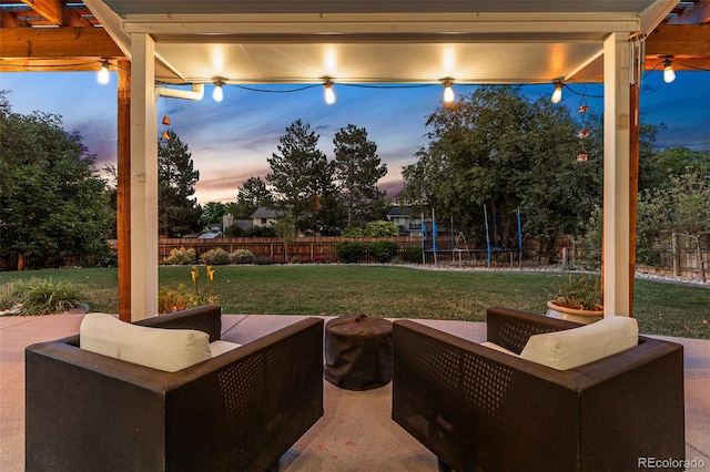 patio terrace at dusk featuring a trampoline and a lawn