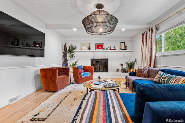 living room featuring beamed ceiling, wood-type flooring, and a brick fireplace