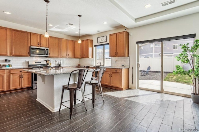 kitchen with stainless steel appliances, wood tiled floor, visible vents, and brown cabinetry