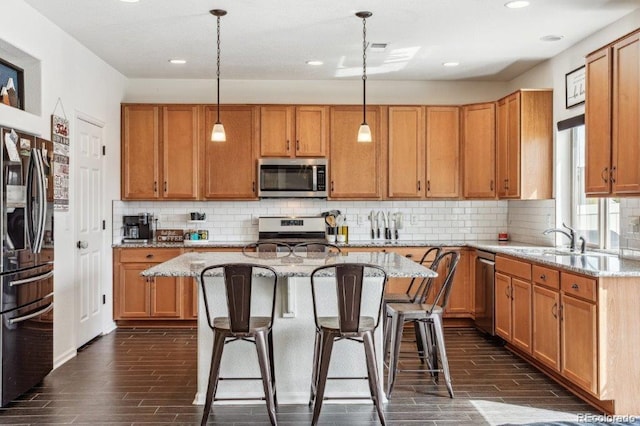 kitchen featuring a center island, wood tiled floor, a kitchen bar, appliances with stainless steel finishes, and a sink