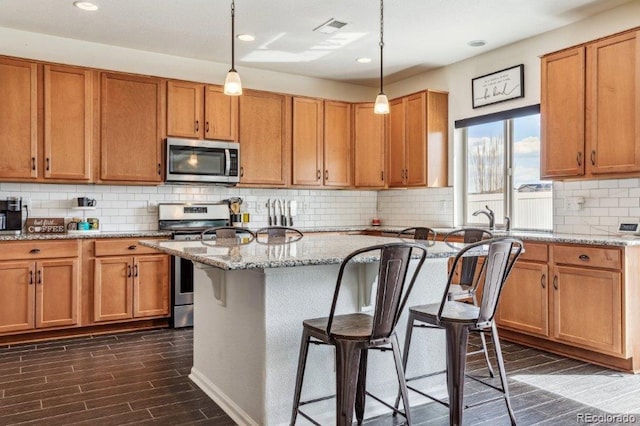 kitchen with visible vents, dark wood-type flooring, light stone countertops, a kitchen breakfast bar, and stainless steel appliances