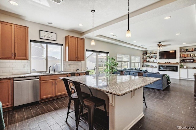 kitchen featuring light stone counters, stainless steel dishwasher, a breakfast bar area, brown cabinetry, and wood tiled floor