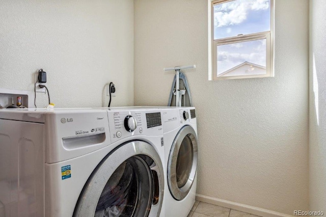 clothes washing area with light tile patterned flooring, laundry area, washer and dryer, and baseboards