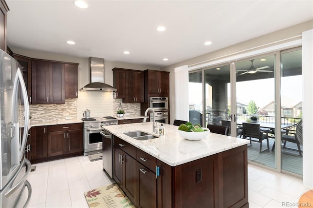 kitchen featuring sink, light stone counters, appliances with stainless steel finishes, wall chimney exhaust hood, and a kitchen island with sink