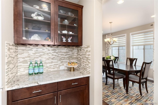 bar featuring pendant lighting, dark brown cabinets, decorative backsplash, and a notable chandelier