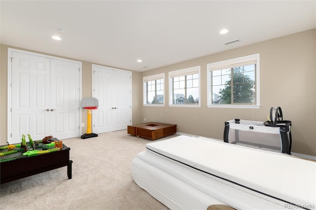 bedroom featuring light colored carpet and two closets