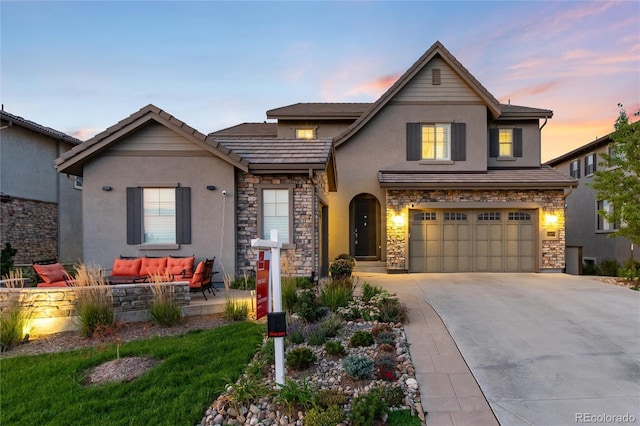 view of front of home with an attached garage, stone siding, concrete driveway, and stucco siding