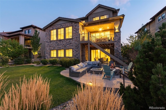 back of property at dusk with a patio, a yard, stone siding, stairway, and an outdoor living space with a fire pit