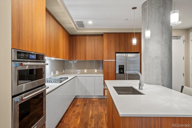 kitchen featuring a kitchen island with sink, dark hardwood / wood-style floors, stainless steel appliances, pendant lighting, and sink