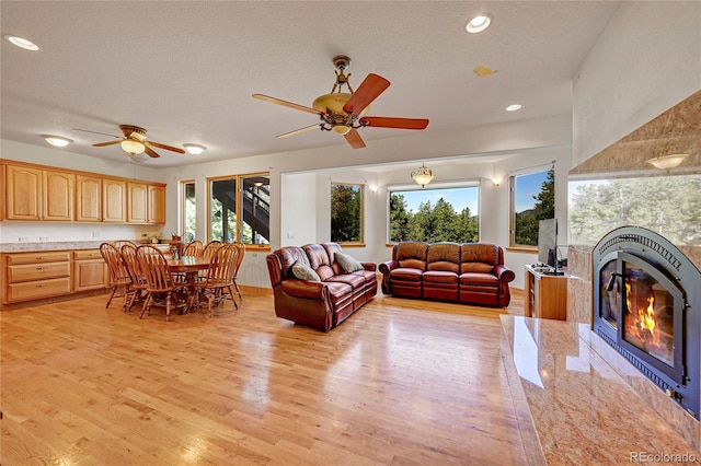 living room featuring ceiling fan, light hardwood / wood-style floors, a textured ceiling, and a tiled fireplace