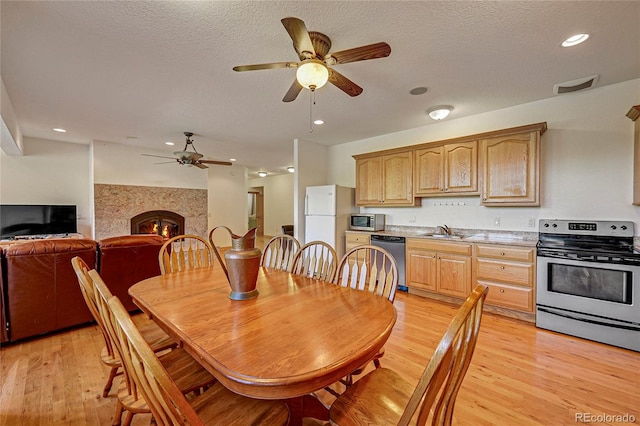 dining space with a tile fireplace, sink, a textured ceiling, and light wood-type flooring