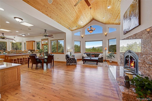 living room with a towering ceiling, wooden ceiling, ceiling fan with notable chandelier, and light wood-type flooring