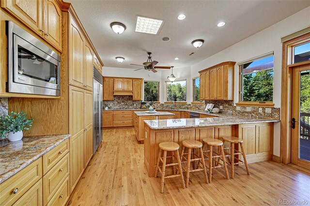 kitchen featuring kitchen peninsula, a breakfast bar, light hardwood / wood-style floors, and appliances with stainless steel finishes