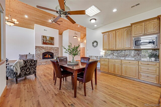 dining room featuring ceiling fan, a high end fireplace, light hardwood / wood-style floors, lofted ceiling, and wood ceiling