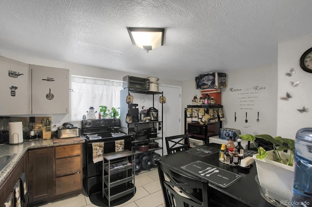 kitchen featuring black electric range oven, light tile patterned floors, and a textured ceiling