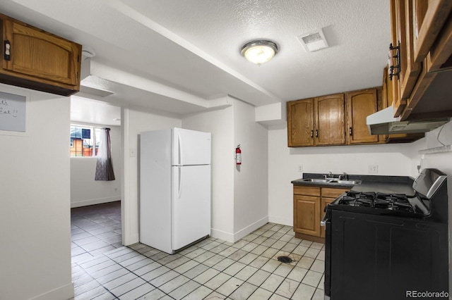 kitchen featuring light tile patterned flooring, stainless steel gas range, sink, a textured ceiling, and white fridge