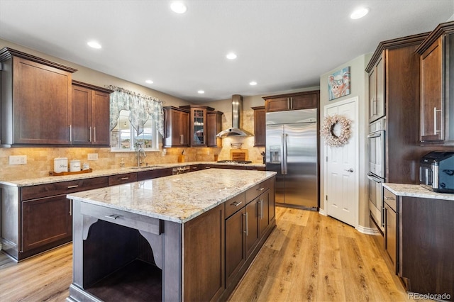 17102 W 85th Pl, Arvada, CO 80007 - kitchen with appliances with stainless steel finishes, wall chimney range hood, light wood finished floors, backsplash, and light stone counters