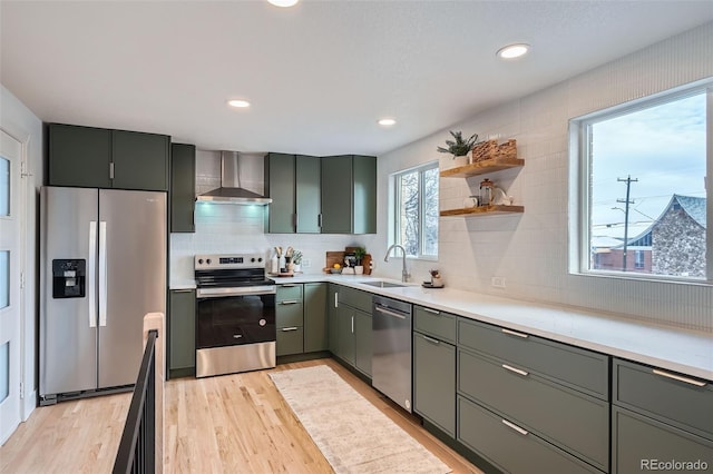 kitchen with light wood finished floors, a sink, appliances with stainless steel finishes, wall chimney exhaust hood, and light countertops